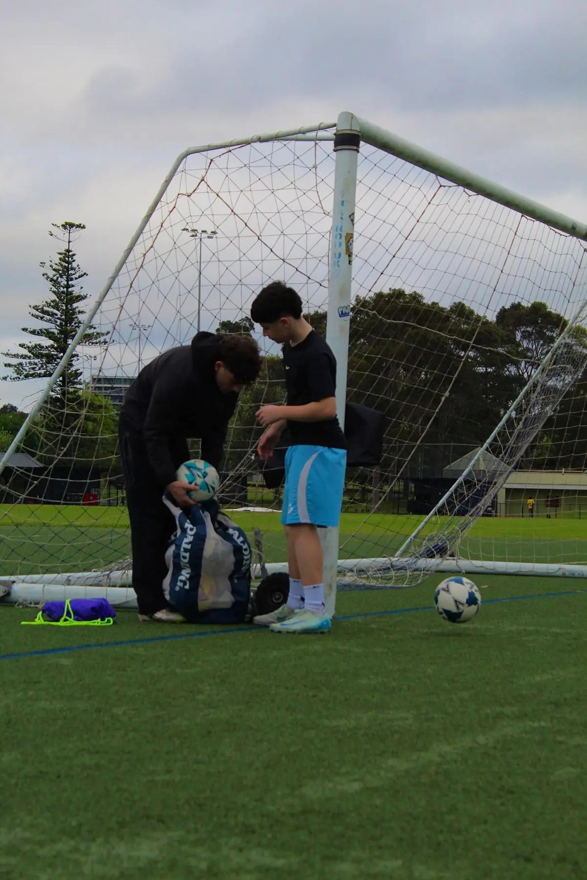 A coach and player setting up balls at the goal