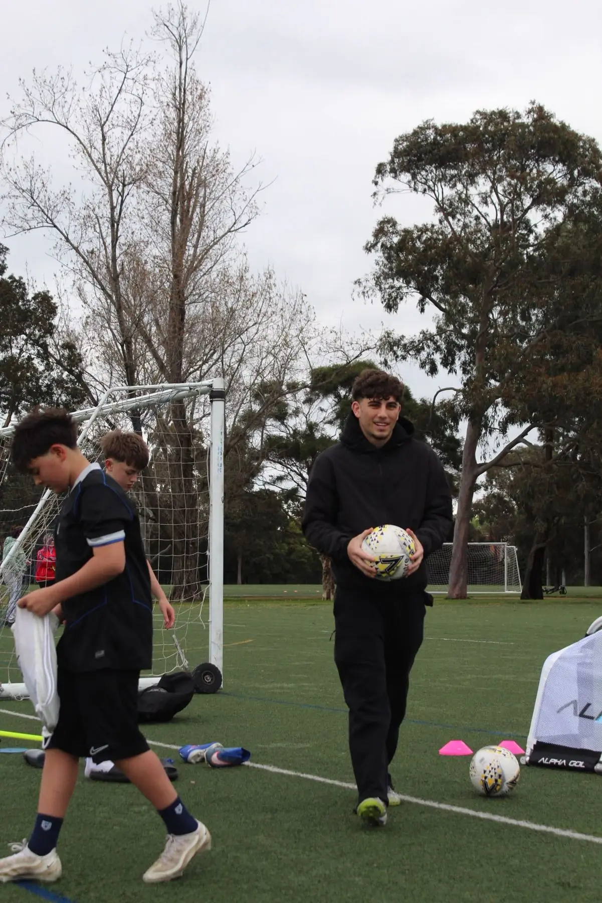 Coach Josh carrying a ball across the training pitch